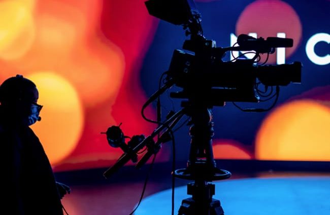 Eine Kamera filmt im Studio. Beim Hybrid Event kann entweder live übertragen oder bereits vorproduziert werden.