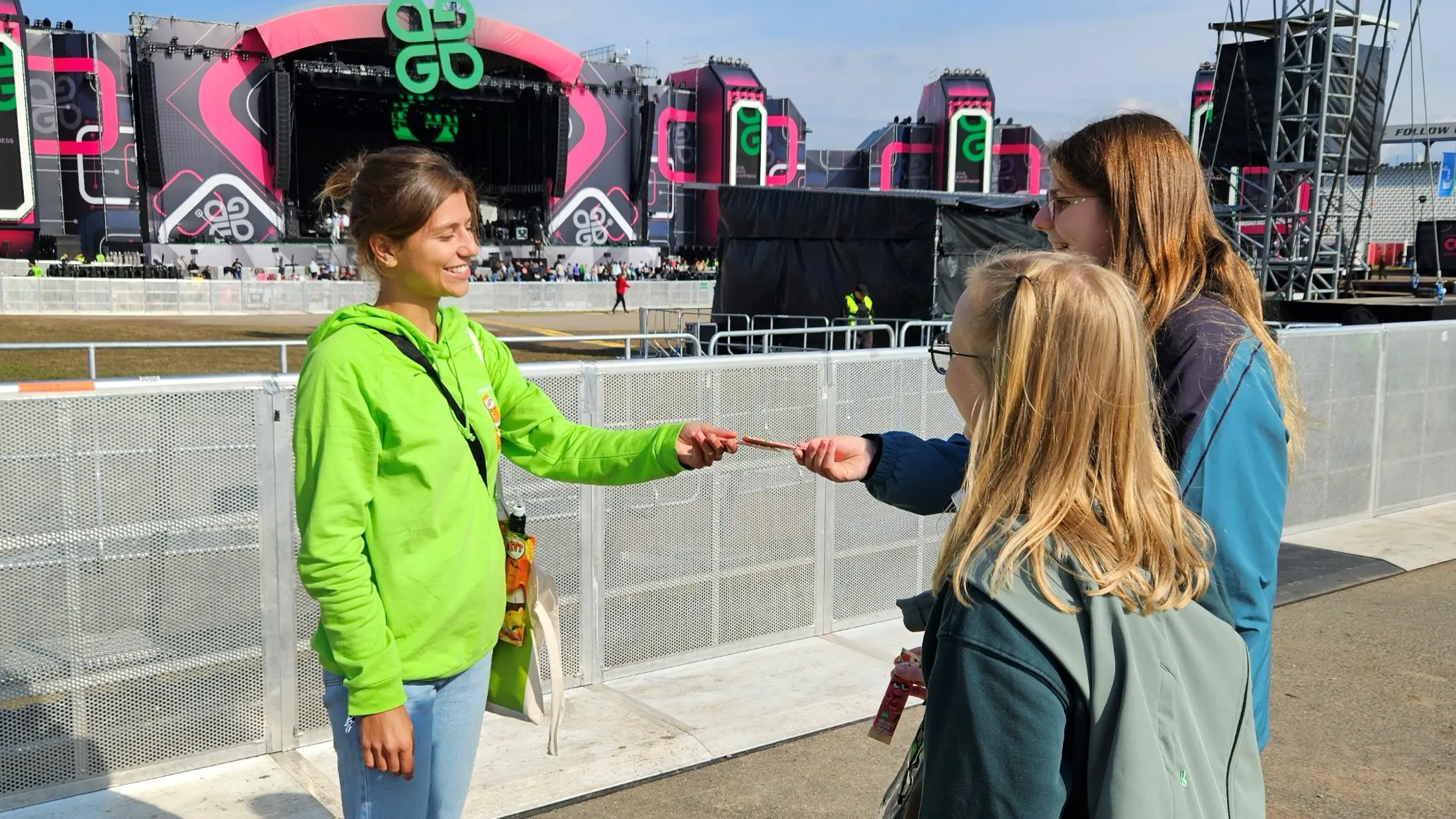 Eine Promoterin übergibt vor der Festivalbühne FRITT-Kaustreifen an zwei Besucherinnen